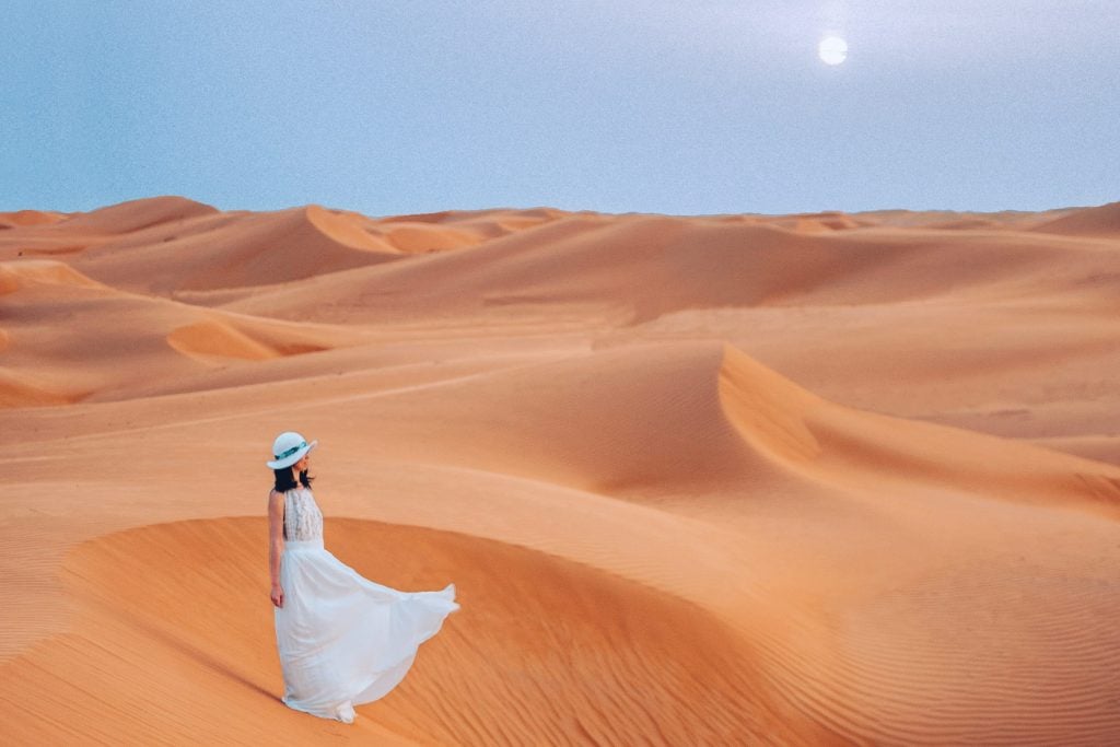 woman wearing a flowy dress standing on wahiba sands desert during her oman itinerary
