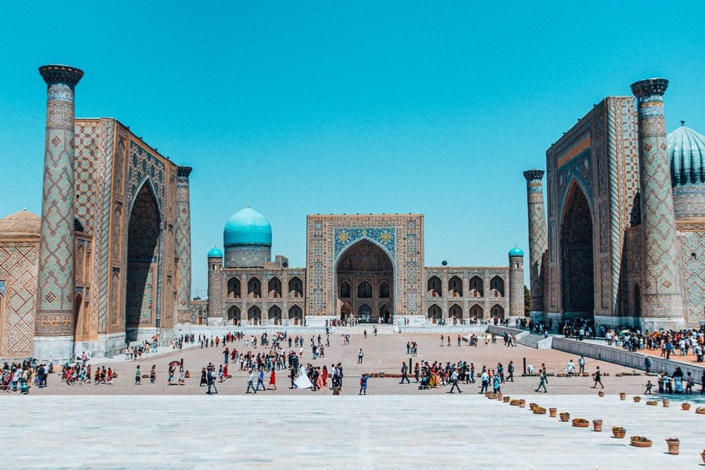 the three madrasahs in registan square filled with tourists in uzbekistan